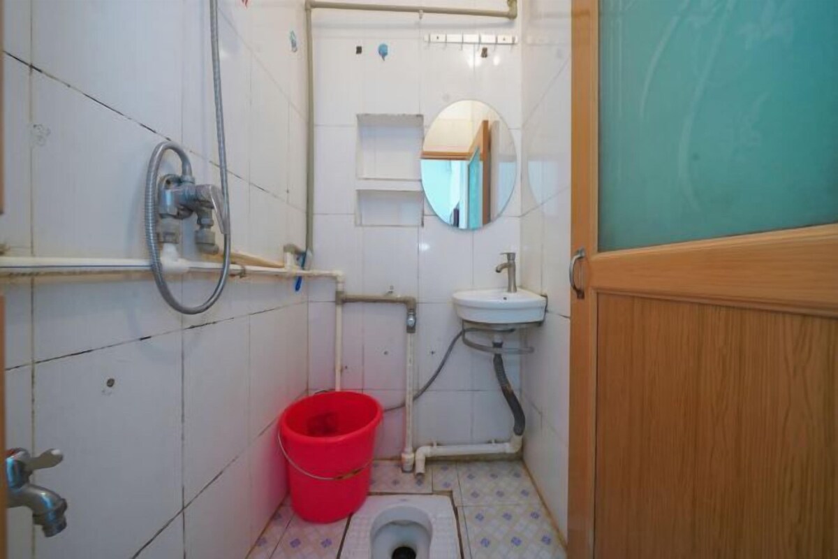 Een kleine badkamer met toilet, wastafel, spiegel en een rode emmer.