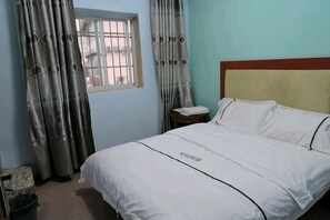 A neatly made bed with a headboard, a bedside table with a phone, and a window with curtains. - Nanning Tianli Hotel (Nanning)