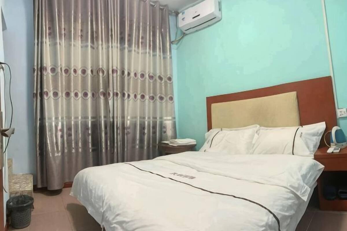 Hotelkamer met een bed, nachtkastje, telefoon, gordijn en een wandairconditioner.