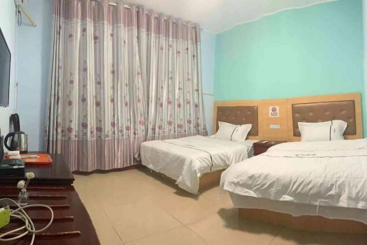Een hotelkamer met twee bedden, een bureau met een waterkoker, en een gordijn met een bloemenmotief.