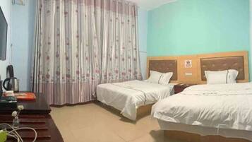 Una habitación de hotel con dos camas, un escritorio con hervidor y una cortina de estampado floral.