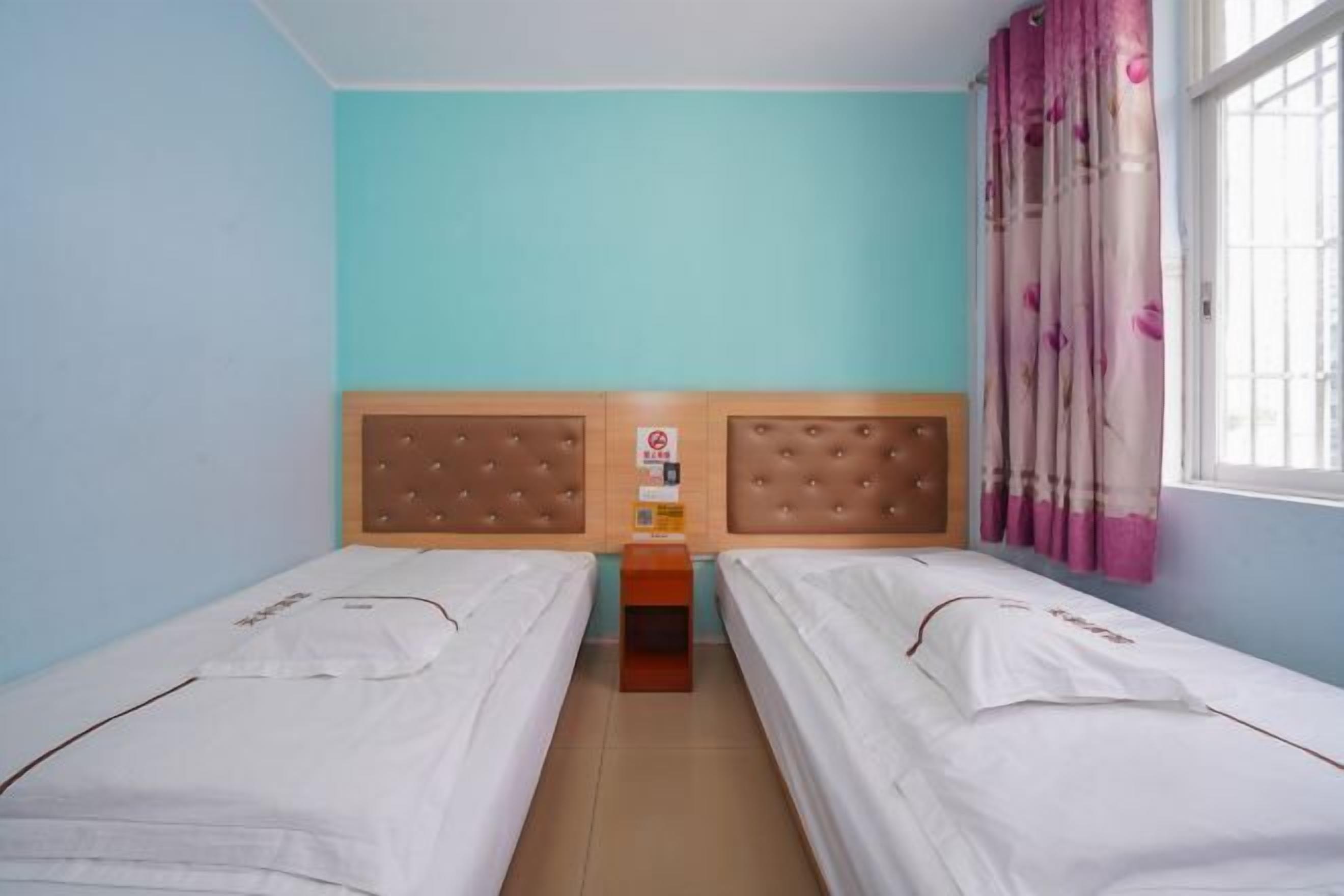 Ein Zimmer mit zwei Einzelbetten, einem Holzkopfstück, einem kleinen Nachttisch und einem Fenster mit rosa Vorhängen.