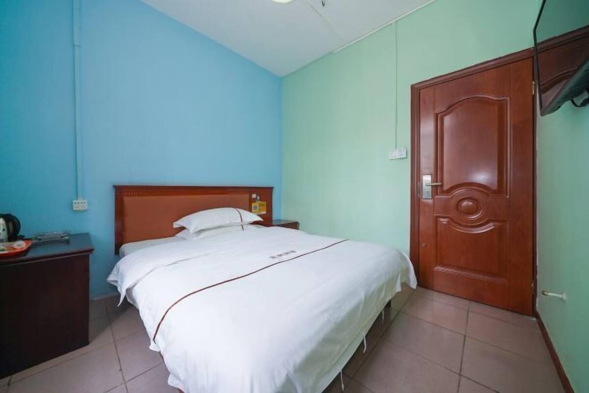 Een slaapkamer met een enkel bed, een houten hoofdbord, een nachtkastje, een houten garderobe en een aan de muur bevestigde televisie.