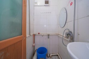 A small bathroom with a white sink, a mirror, and a shower. There is a blue bucket on the floor. - Nanning Tianli Hotel (Nanning)