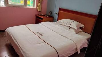 Ein Einzelbett mit Holz-Kopfstück, ein Nachttisch mit Lampe und ein Fenster mit Vorhang.