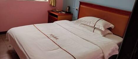 Una cama individual con cabecera de madera, una mesita de noche con lámpara y una ventana con cortina.