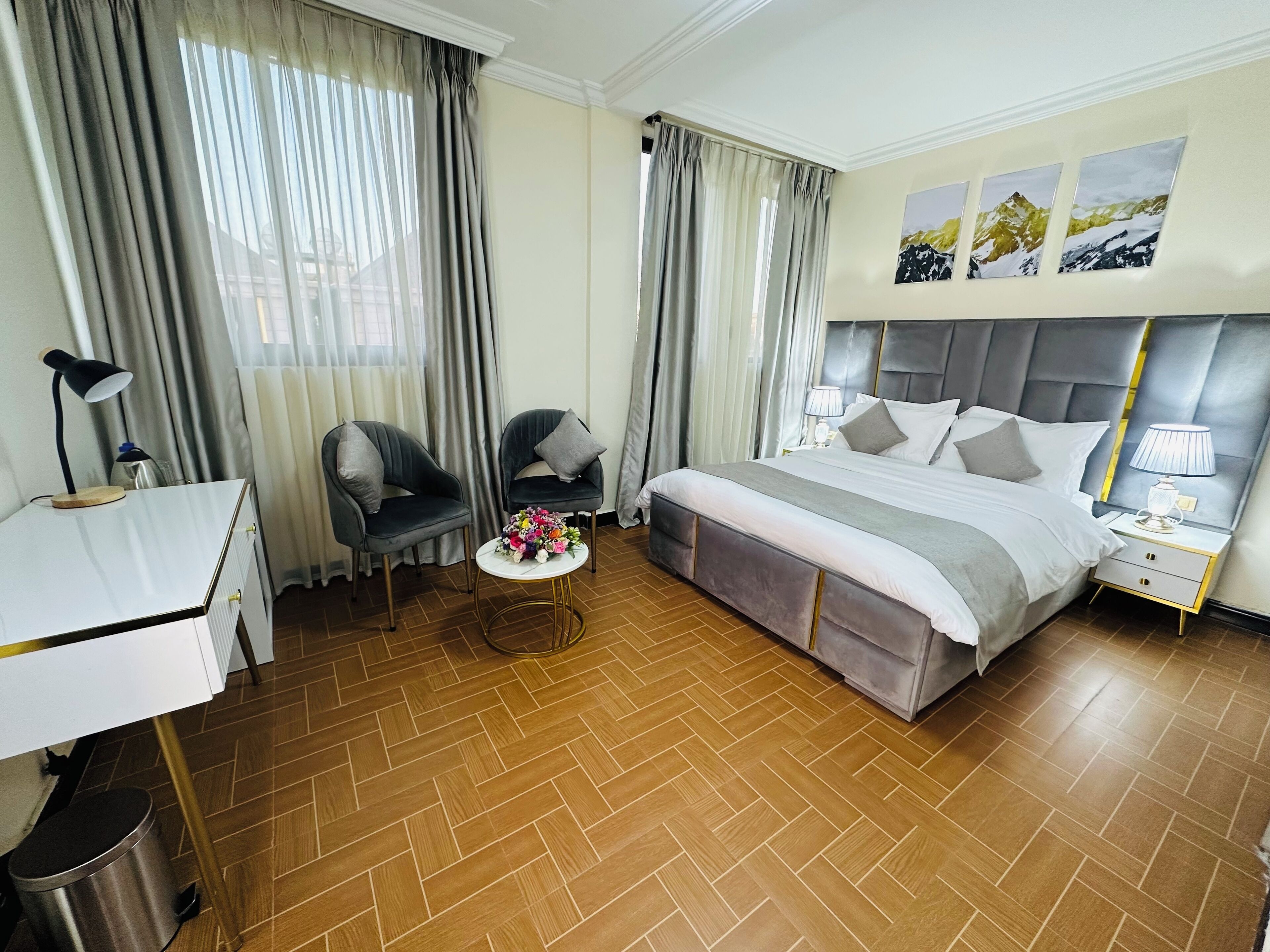 A hotel room with a bed, two armchairs, a small table with a bouquet, a desk with a lamp, and a trash bin.