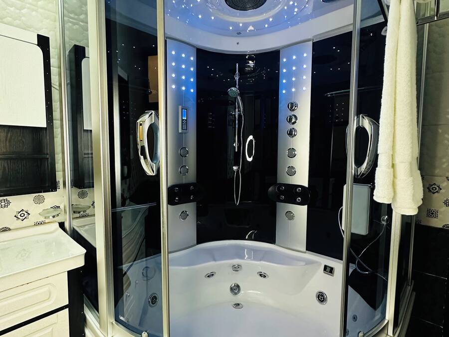 Un jacuzzi moderno, rodeado de vidrio, con un panel de control y un cabezal de ducha integrado.