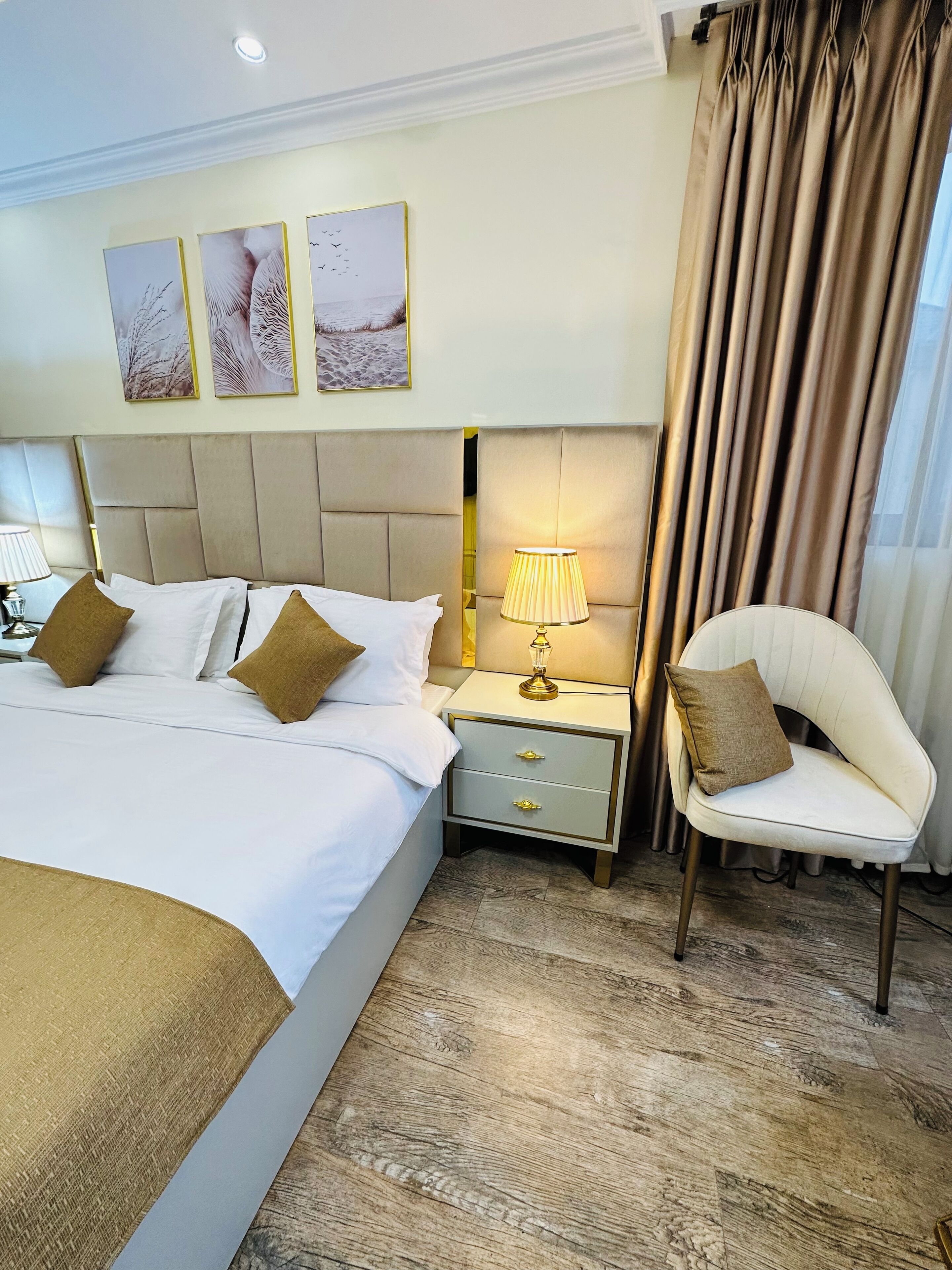 A hotel room with a large bed, a bedside table with a lamp, a chair, and three framed pictures on the wall.