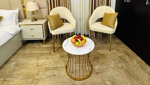 A hotel room with a bed, two armchairs, a small table with fruit, a nightstand, a lamp, and a large window with curtains. - Calm Corner Addis  (Addis Ababa)