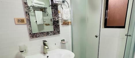 Un bagno con un lavandino bianco, uno specchio con cornice decorativa, box doccia in vetro e un portasciugamani con asciugamani.