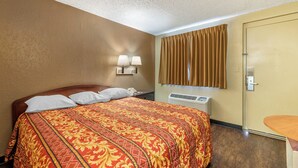 A hotel room with a large bed, two bedside lamps, a window with curtains, and a wall-mounted heater. - Pueblo Inn (Pueblo)