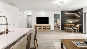 A modern kitchen with a large island, wooden cabinets, and a flat-screen TV. - Santos Place -New Built Home -4Mins To Trailhead- Centrally Located! (Ocala)