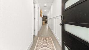 A hallway with a patterned rug, white walls, and a black door with frosted glass panels. - Santos Place -New Built Home -4Mins To Trailhead- Centrally Located! (Ocala)