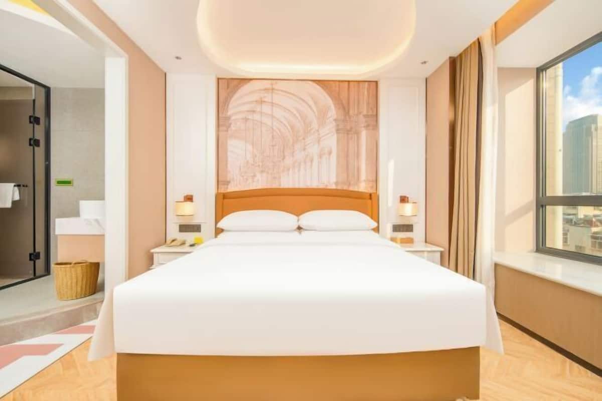 Une chambre d’hôtel avec un grand lit, une tête de lit ornée d’une fresque, des lampes de chevet, une fenêtre donnant sur un beau paysage et un plancher en bois.