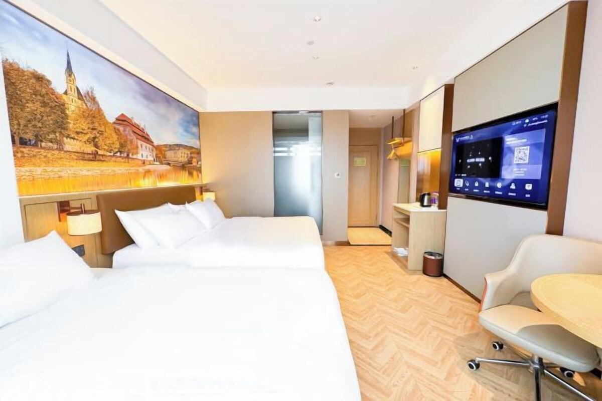 Habitación de hotel con cama, escritorio, silla, televisor y un cuadro de un paisaje.