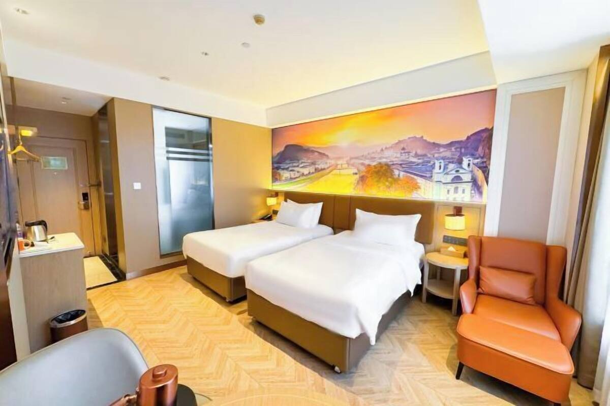 Une chambre d’hôtel avec deux lits, une chaise, un bureau avec une lampe et un tableau au mur.