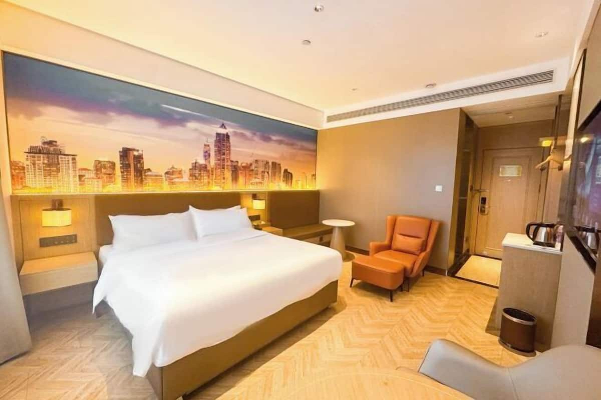 Une chambre d’hôtel avec un grand lit, un tableau représentant un paysage urbain, une chaise et un téléviseur.