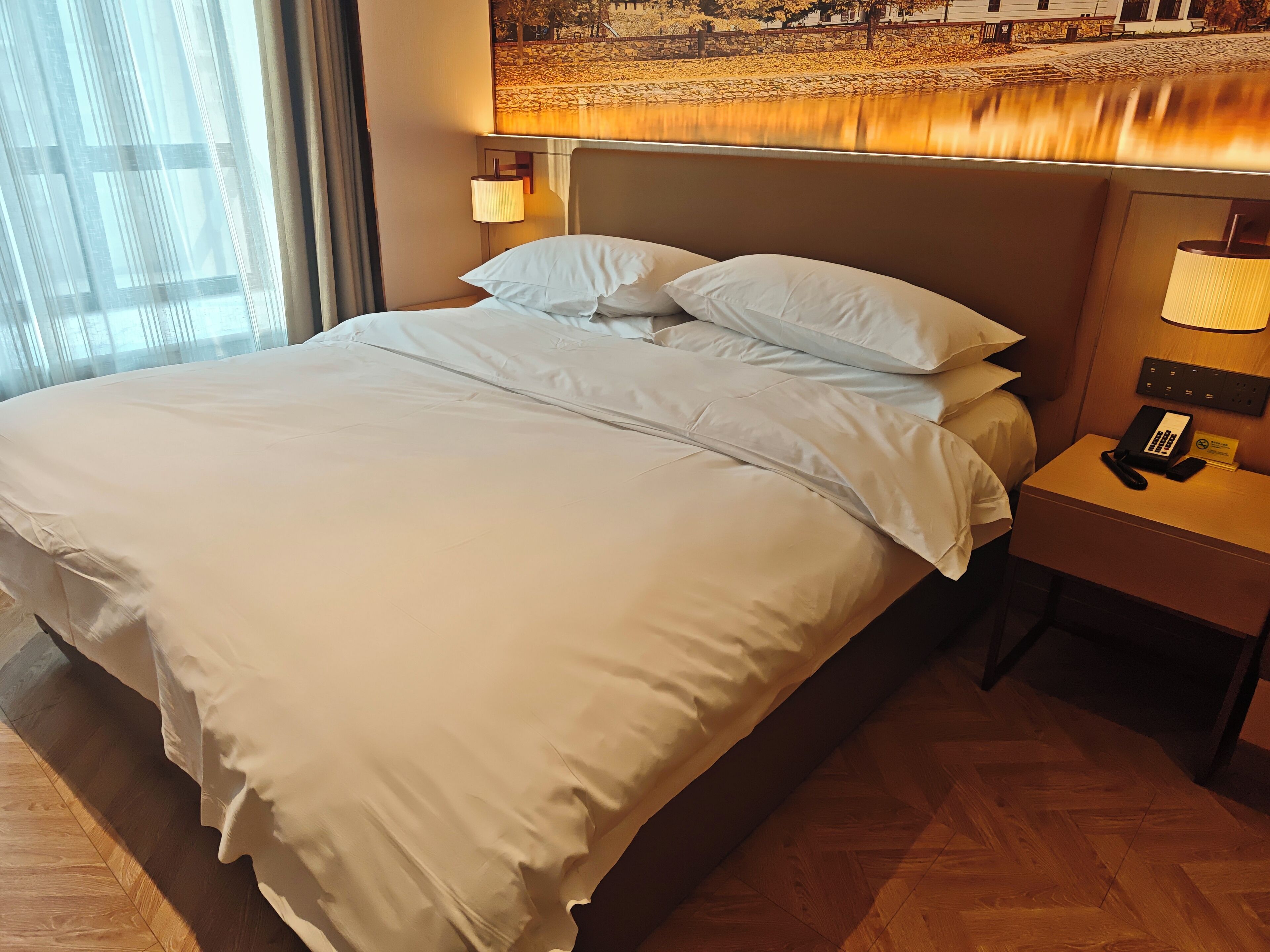 Une chambre d’hôtel avec un lit bien fait, une table de chevet avec un téléphone et un bloc-notes, et une lampe fixée au mur.