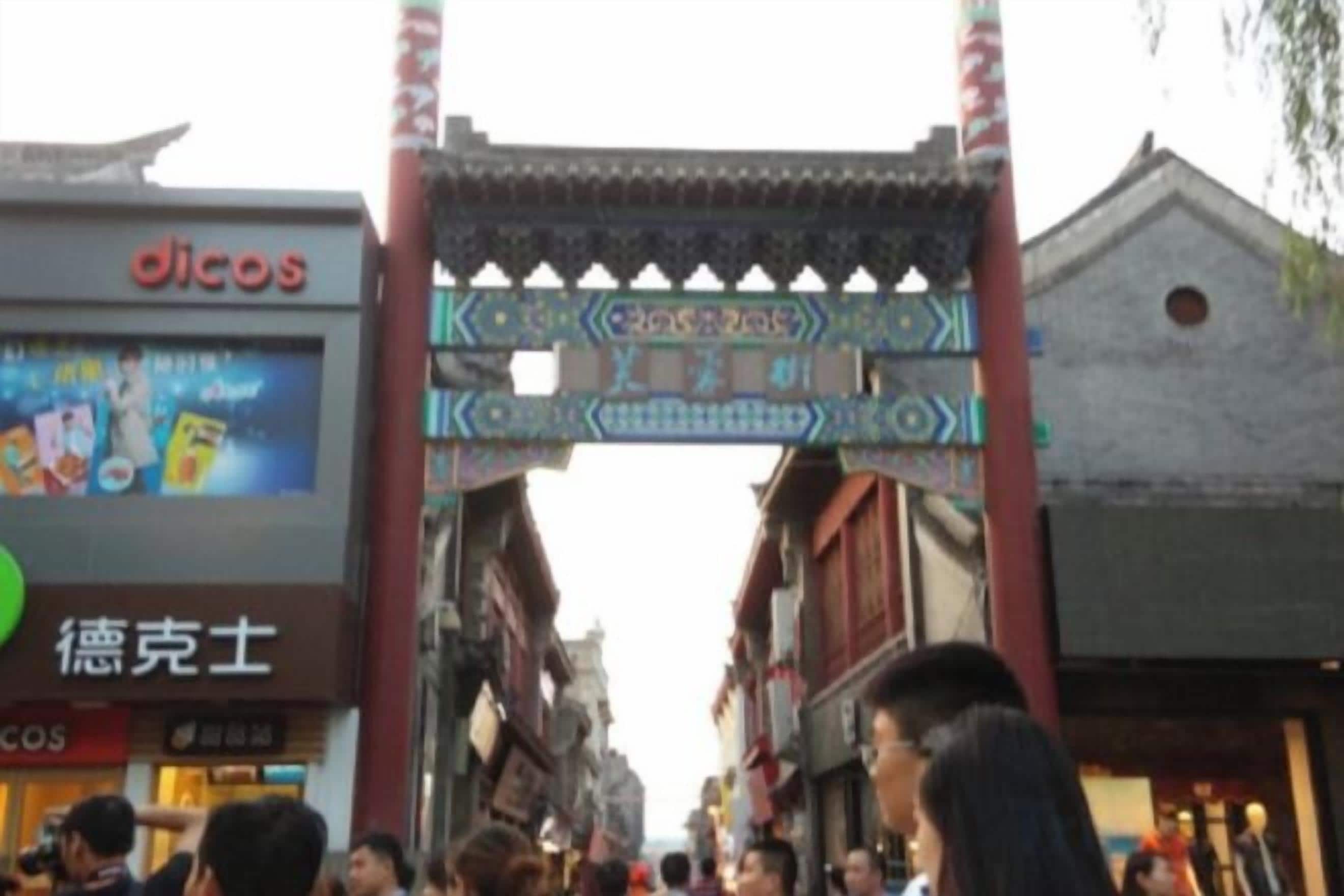 A traditional gate with intricate designs, a sign for 'dicos' on the left, and a building with a traditional roof on the right.