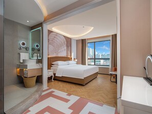 Habitación de hotel moderna con una cama grande, baño con espejo y lavamanos, y vista de la ciudad a través de la ventana.