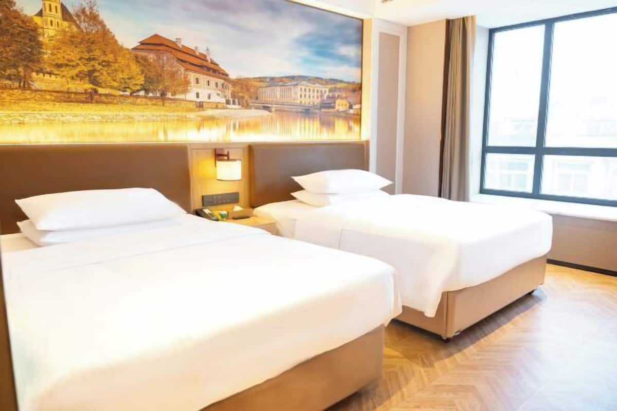 Une chambre d’hôtel avec deux lits, une grande fenêtre et un tableau représentant un paysage.