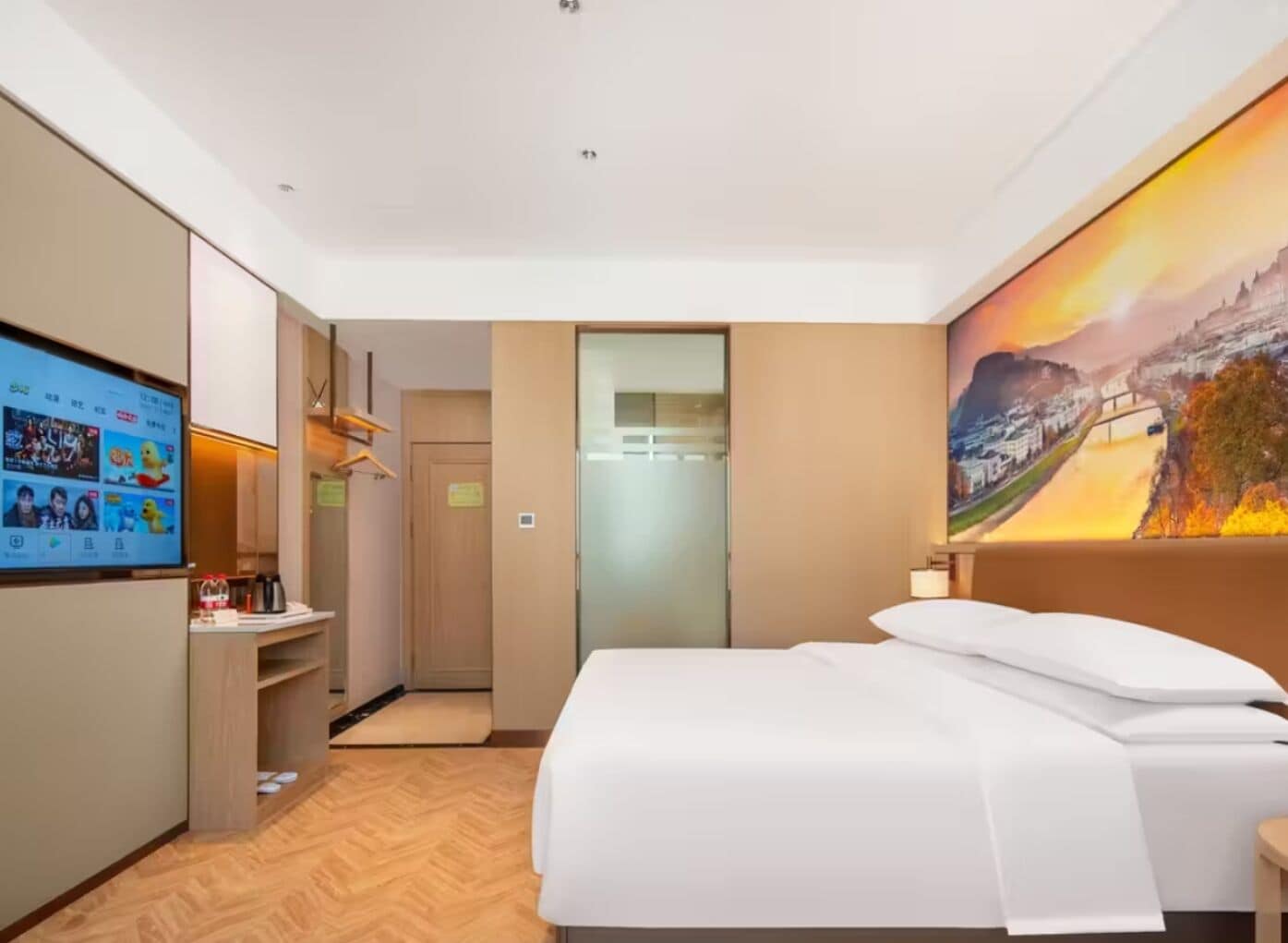 Habitación de hotel con cama, televisor mostrando un video, un cuadro en la pared y suelo de madera.