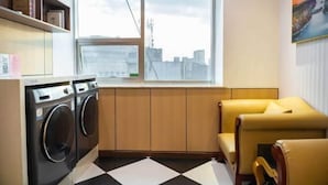 A compact laundry room with a large window, a washing machine, and a yellow armchair. - Vienna Hotel (Jinan Huayuan Road ) (Jinan)