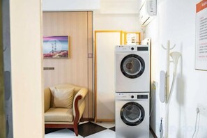 A compact laundry room with stacked washing machines, a chair, and a wall-mounted drying rack. - Vienna Hotel (Jinan Huayuan Road ) (Jinan)