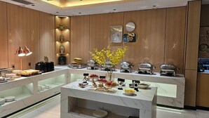 A modern kitchen with marble countertops, wooden cabinets, and a central island with a vase of yellow flowers. - Vienna Hotel (Jinan Huayuan Road ) (Jinan)