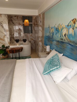 Habitación de hotel moderna con una cama grande, un cuadro de caballos, una pared de mármol y un baño con bañera y lavamanos.