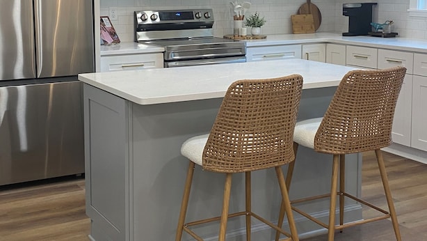 Une cuisine moderne avec des meubles blancs, des appareils en acier inoxydable, un îlot central doté de tabourets de bar et un lustre décoratif.