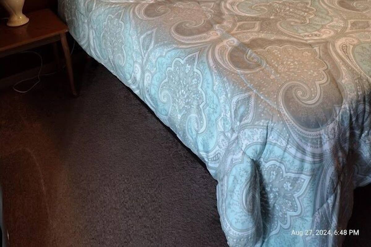 A neatly made bed with a patterned bedspread, a bedside lamp, and a framed picture on the wall.