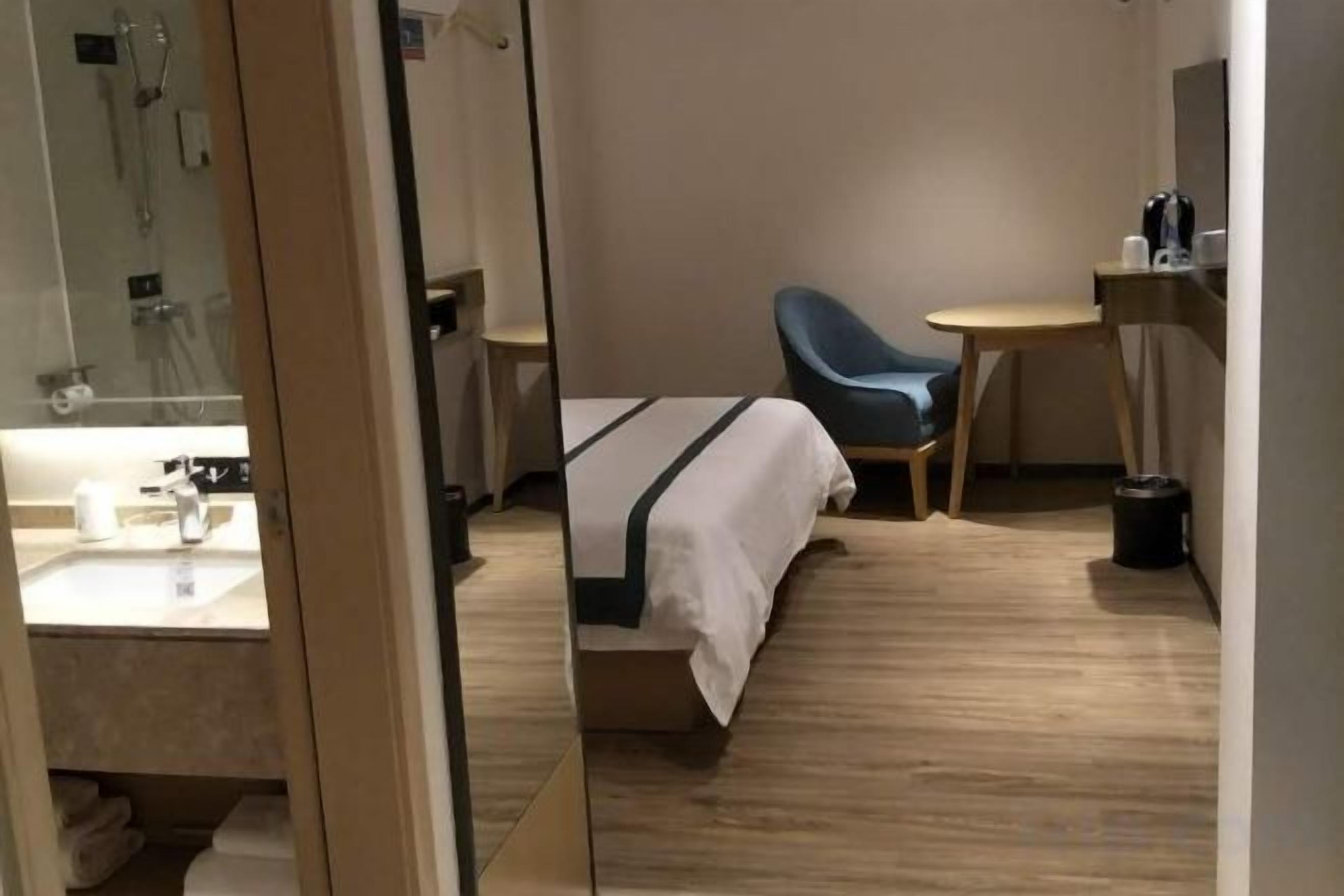 A hotel room with a bed, a chair, a small table, and a mirror.