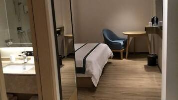 A hotel room with a bed, a chair, a small table, and a mirror.