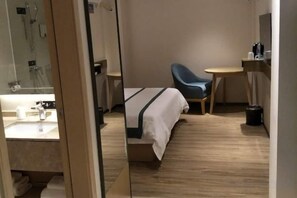 Hotellihuone, jossa on sänky, tuoli, pieni pöytä ja peili.