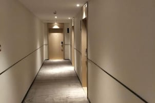 Un pasillo estrecho y bien iluminado con piso alfombrado, que conduce a una puerta al final.