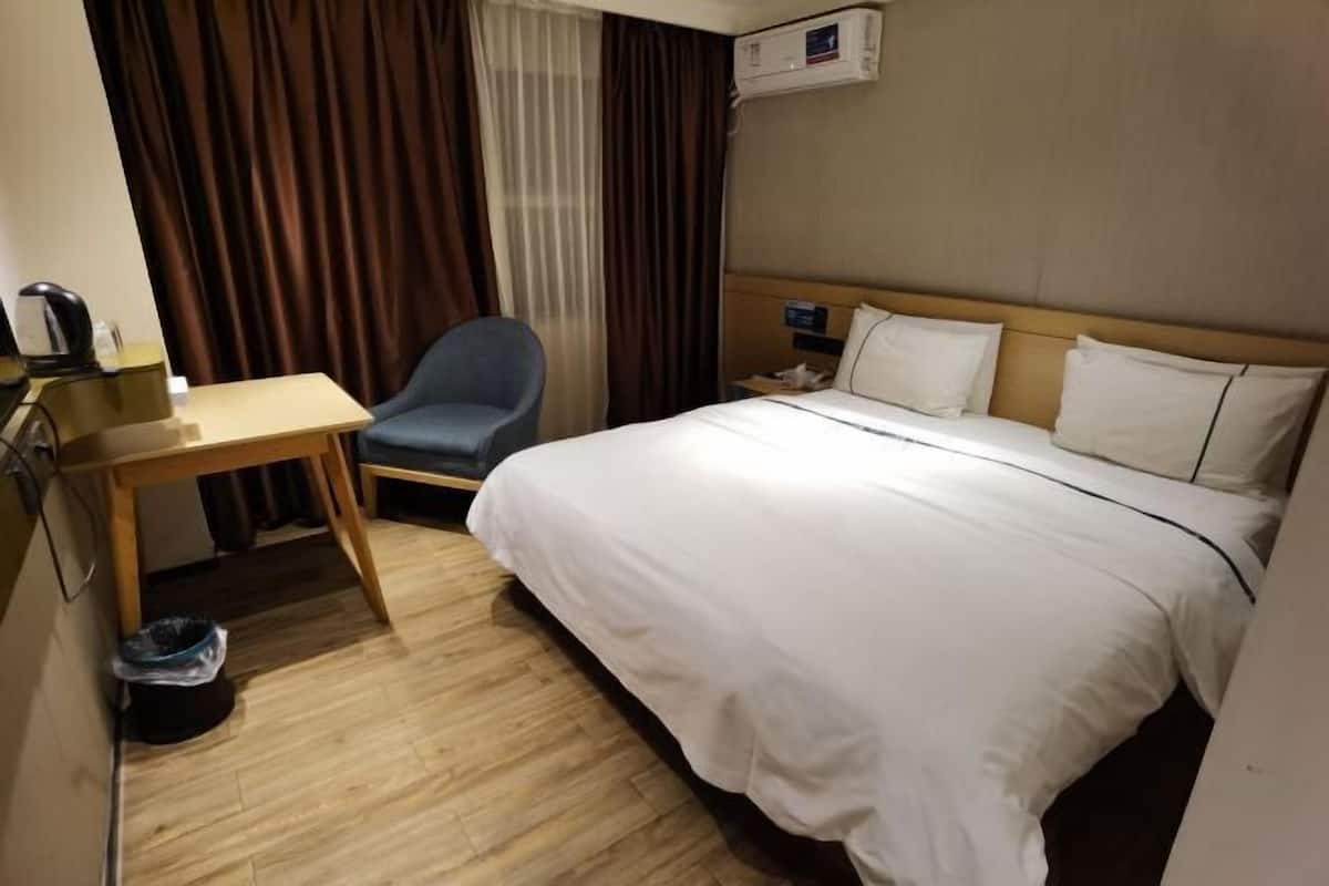 A hotel room with a bed, a desk, a chair, and a trash bin.