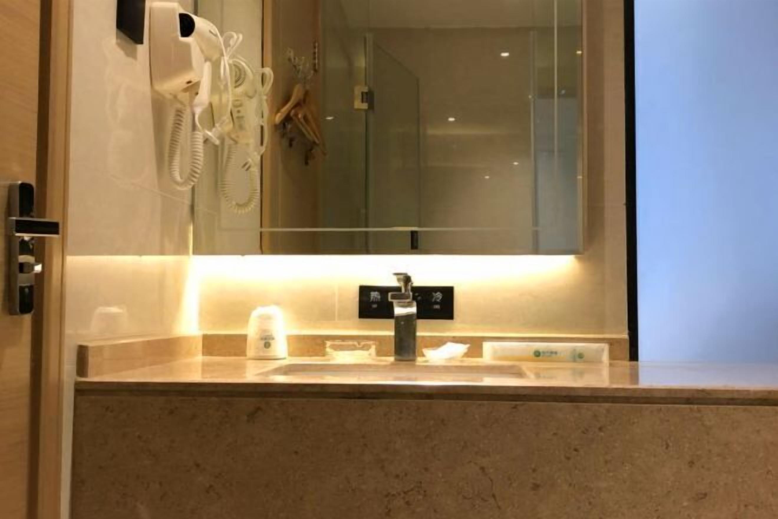 A hotel bathroom with a sink, a mirror, a hairdryer, and a glass shower enclosure.