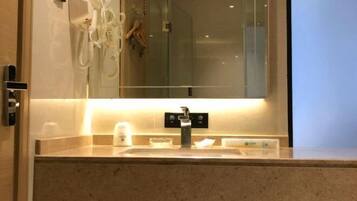 A hotel bathroom with a sink, a mirror, a hairdryer, and a glass shower enclosure.