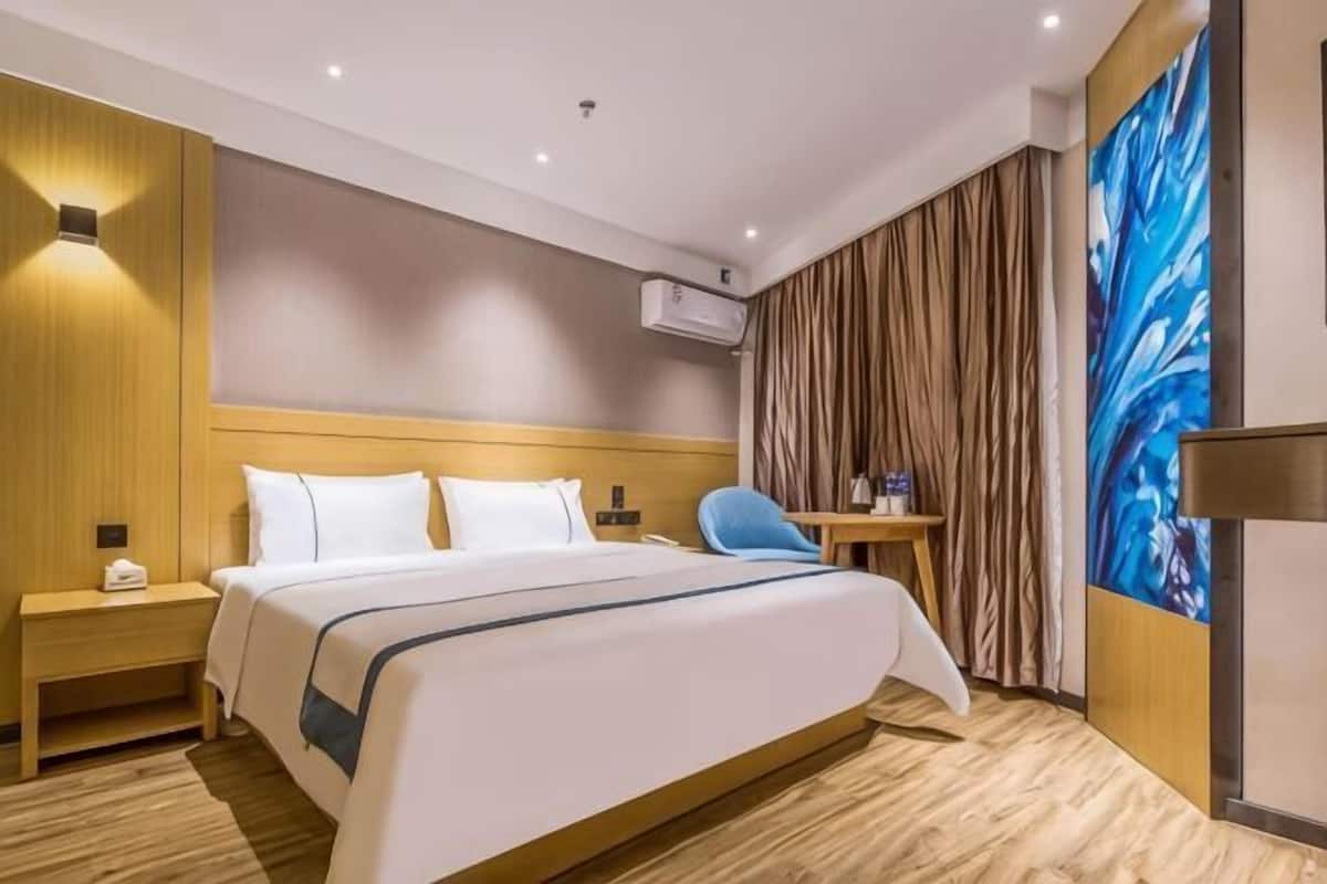 A hotel room with a large bed, a nightstand, a chair, a desk, and a painting on the wall.