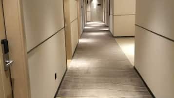 Un pasillo de hotel con piso alfombrado, puertas a ambos lados y una señal de salida verde al final.