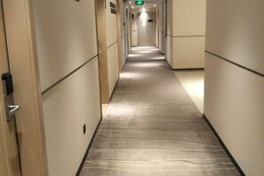 A hotel corridor with a carpeted floor, doors on either side, and a green exit sign at the end. - City Comfort Inn (Yunfu Yu'nan Ducheng) (Yunan)
