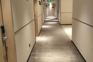 Un pasillo de hotel con piso alfombrado, puertas a ambos lados y una señal de salida verde al final.