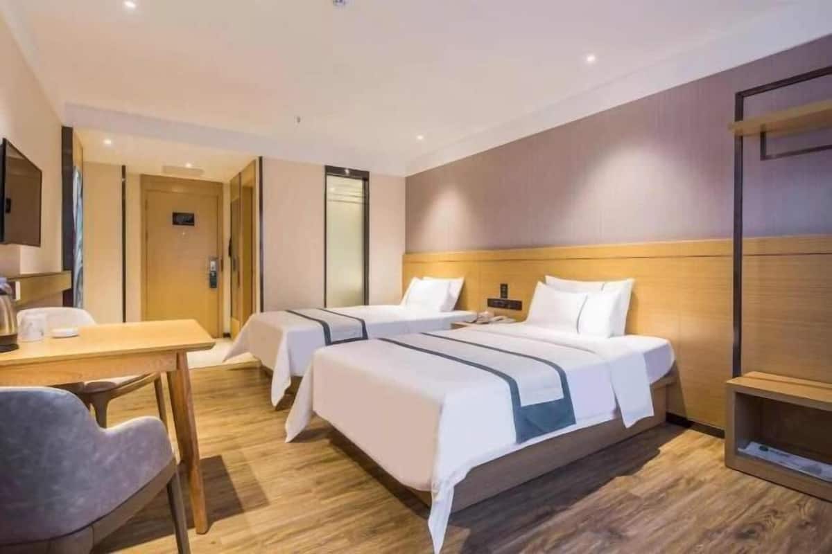 A hotel room with two beds, a desk, a chair, and a television.