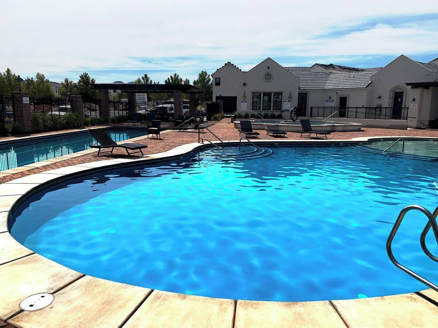 A swimming pool with lounge chairs and a brick pathway leading to a building with a triangular roof.