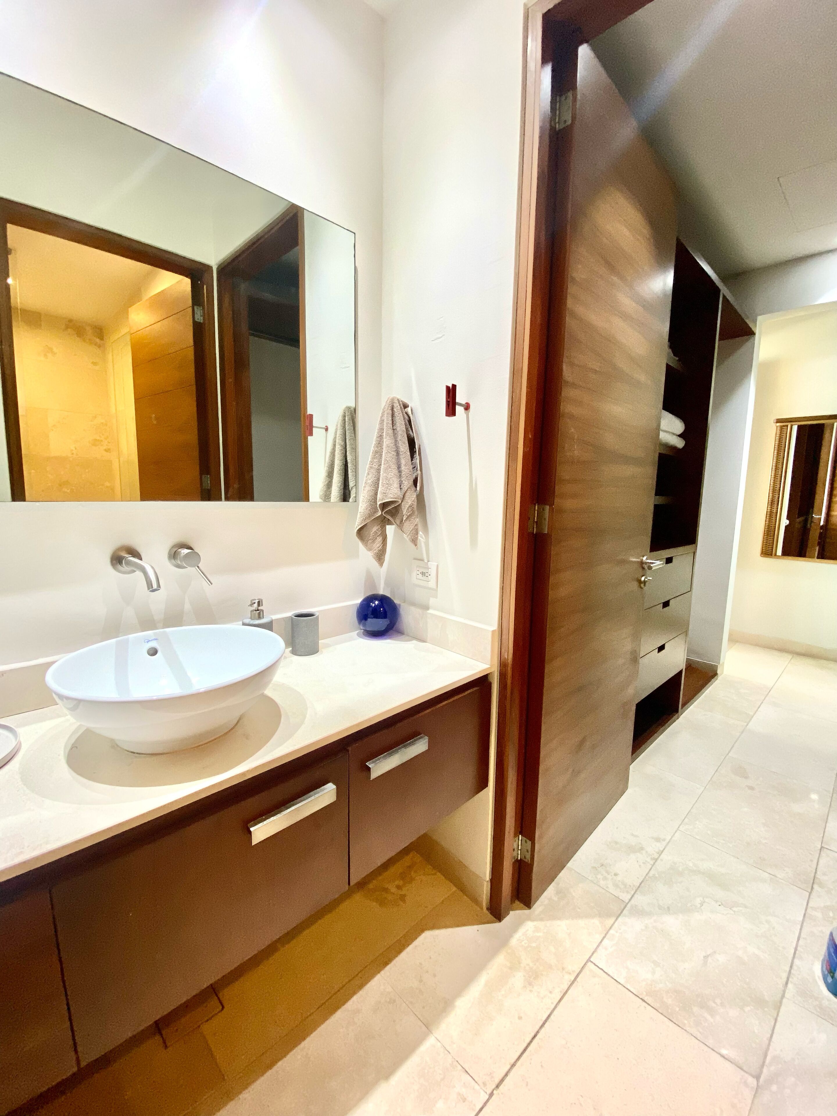 A modern bathroom with a large mirror, a white sink, and a wooden vanity.
