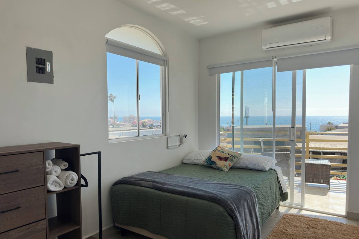 A bedroom with a bed, a wardrobe, a window, and a balcony with a view of the sea.