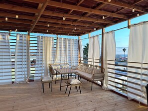 Un espace extérieur aménagé avec une table et des chaises en bois, surmonté d’un toit en bois et agrémenté de luminaires suspendus.
