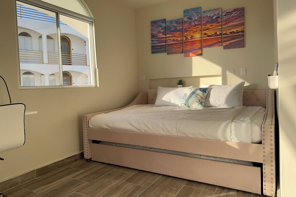 A bedroom with a bed, a window, and a wall with three paintings.